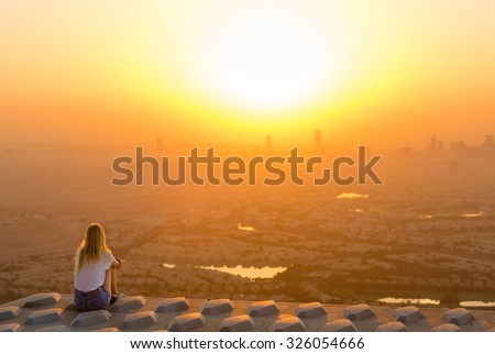 Woman sitting on top of skyscraper overlooking the city at sunrise
