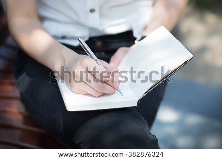 Closeup of a female hand writing on an blank notebook with a pen.
