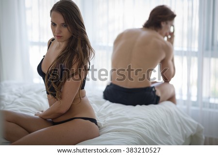 Unhappy couple sitting in bed away from each other. Woman in foreground.