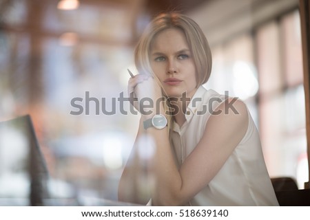 Thoughtful concept. Woman working on a computer at a cafe while gazing through the window glass.