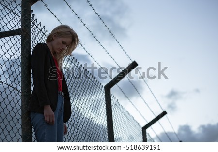 Sad woman standing alone against barbwire fence.