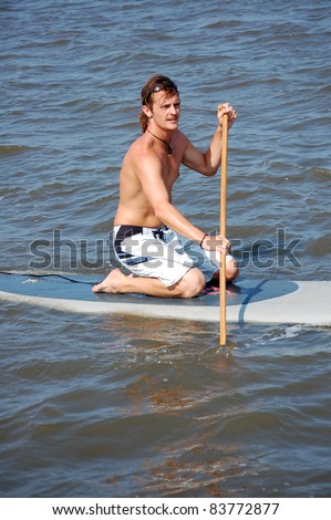 A young man kneels on his stand-up paddle-board