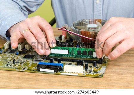 Young caucasian repairman working in computer store, repairing computer and adding ram to pc. Focus on RAM memory,
