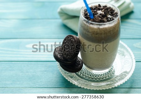Milkshake (chocolate smoothie)  in a glass on colorful turquoise blue painted wooden boards. Selective focus on cookies
