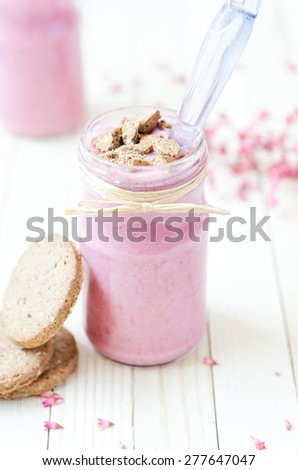 Pink Strawberry Smoothie in retro jar with purple flowers and brown cookies on light rustic boards.
