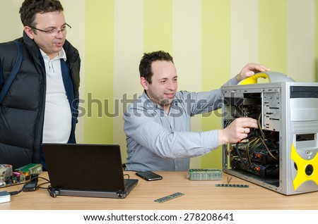 Happy computer engineer repairing broken computer while conversing with male customer at the office. Isolated on retro striped green and yellow wallpaper.