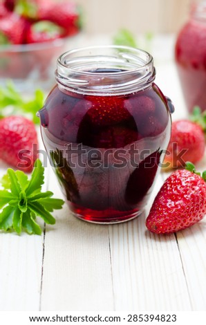 Strawberry jam in a jar and fresh strawberries on the light wooden table