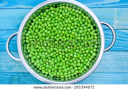 Fresh raw baby peas in small colander, over colorful turquoise blue painted wooden boards.