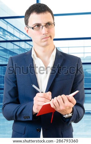 Young business man taking notes for the next meeting looking confused over big office\'s windows background