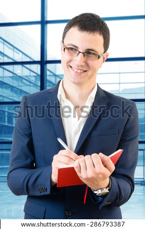 Young business man taking notes for the next meeting looking happy over big office\'s windows background
