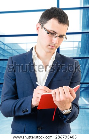Young business man taking notes for the next meeting over big office's windows background