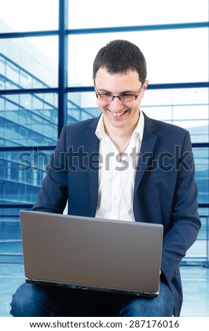 Young businessman wearing glasses and waiting for the plane watching football game on the airport with laptop in his lap