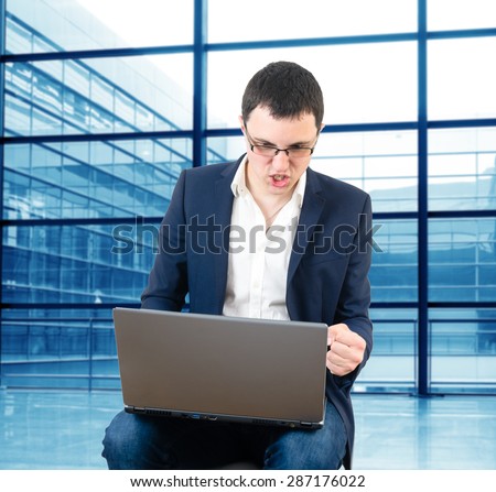 Young businessman wearing glasses and waiting for the plane watching football game on the airport with laptop in his lap