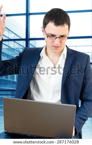 Young businessman wearing glasses and holding his head on the airport with laptop in his lap