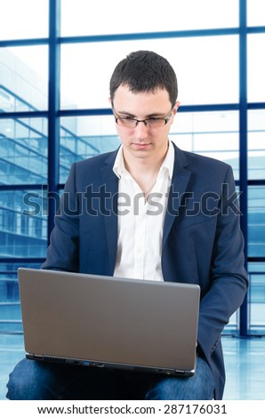 Young businessman wearing glasses and waiting for the plane watching foodbal game on the airport with laptop in his lap