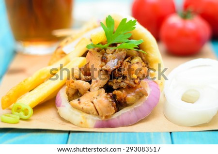 Plate of traditional Greek gyros with meat, fried potatoes, tomato, onion and drink on brown Paper, Placed on blue Wooden Table