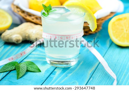 Cold glass of lemonade with ice, lemon and ginger on colourful turquoise blue painted wooden boards
