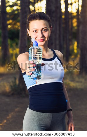 Girl holding a bottle of water offering you to drink after workout in the forest.