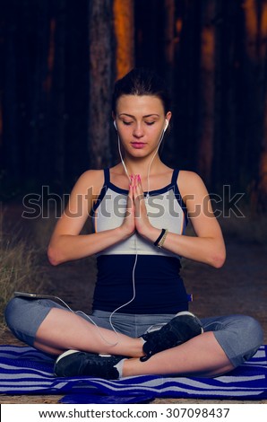 Young woman meditating in forest while listening to the music as the sun goes down. Soft focus, shallow DOF, low light, some visible noise