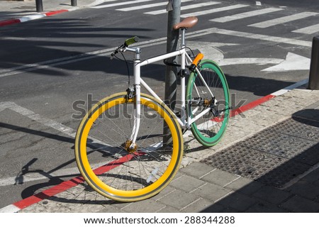 A colored bicycle locked to a post on the pavement
