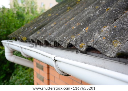 House asbestos roof with close up gutter holder and plastic roof gutter pipe. Guttering.