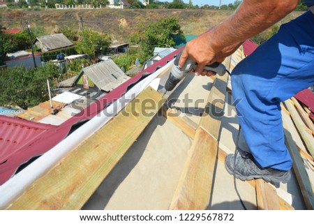 Roofing contractor installing metal roof tile for roof repair. Roofer install metall roof sheets with screw driver on the rooftop.