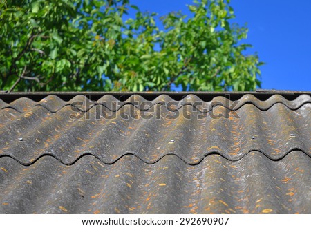 Blue sky over the dangerous asbestos old roof tiles able to use as textured background. Asbestos has not been used in domestic building materials since the 1980.