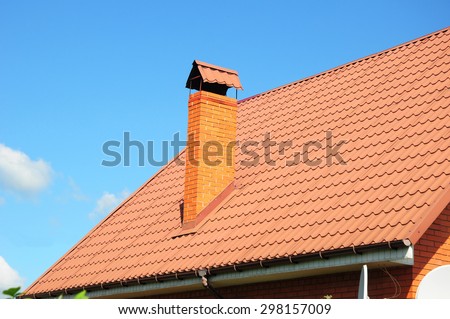 Faded red metal roof tile, rain gutter and chimney against blue sky. Bad roofing.