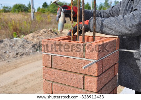 Bricklayer Worker Installing Red Clinker Blocks around Iron Bar and Caulking Brick Masonry Joints Exterior Wall with Trowel Putty Knife and Fixing with Spirit Level Outdoor