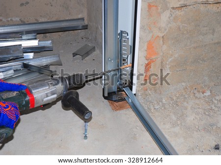 Garage Door Installation. Worker Using Drill to Attach  Plastic and Metal Profile Door Panel to Wall.