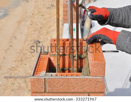 Bricklaying Closeup. Bricklayer hand holding a Putty Knife and Building a Brick Wall Column with Iron Bar Outdoor.