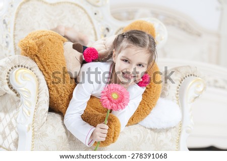 Happy girl with teddy bear and flower on armchair