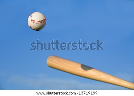 Baseball about to be struck by baseball bat with blue sky background.