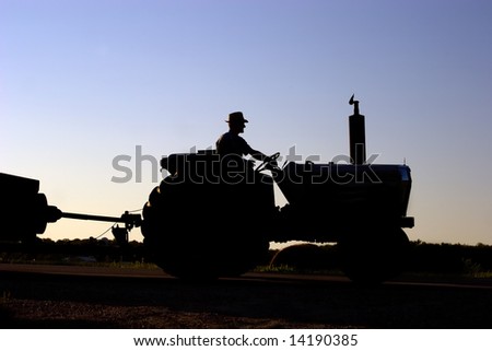 Silhouette of farmer on tractor with sun setting in background.