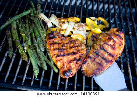 Chicken, peppers and asparagus on a barbecue with a lifter lifting the chicken breast.