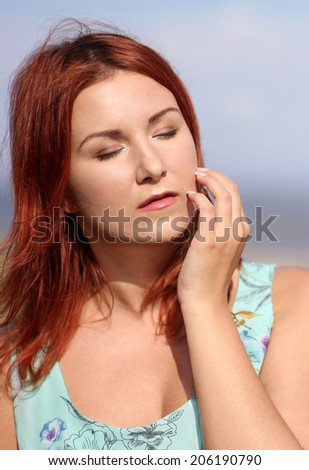 Redhead girl with closed eyes enjoying summer sunlight and wind at the seashore