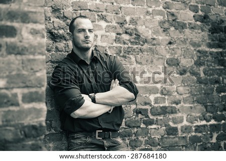 Man posing outside, leaning on a brick wall.