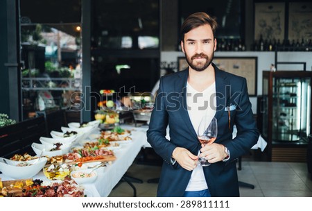 Young elegant man standing in the restaurant, holding a glass of wine. Man\'s style