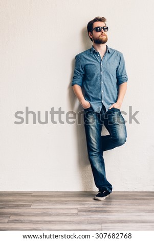 Young handsome man with sunglasses,  leaning against a white wall.