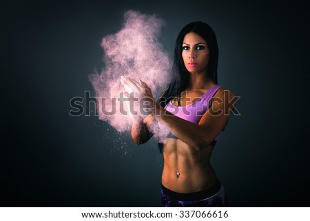 Athletic young woman clapping hands with powder. Studio shot.