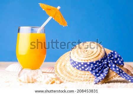 Glass of orange drink and straw hat at the sand beach
