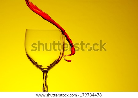 Red wine splash in crystal glass on yellow background.