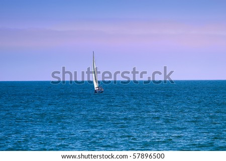 Sailboat on the ocean against dusk sky of blue and pink.