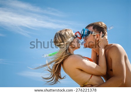 Happy young couple with snorkeling gear. Beach couple having fun on vacation travel with mask . Young couple with the diving masks kissing on a beach.Couple under blue sky.