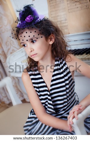 Beautiful girl in a striped dress with a lilac hat near the piano