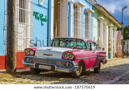 TRINIDAD, CUBA - DECEMBER 8, 2013: Purple and white classic American car and blue colonial building in streets of Trinidad, where old cars are relic of Cuban revolution and still attracts tourists.