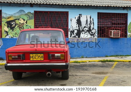 VARADERO, CUBA - DECEMBER 11, 2013:Red classic American car and colorful wall paintings presenting remnants of the Cuban Communist Revolution.