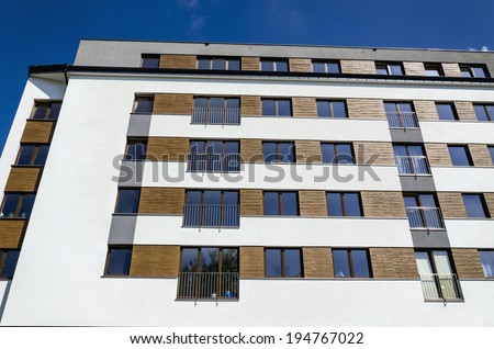 A view of a modern white apartment building, white facade decorated with wood against blue sky