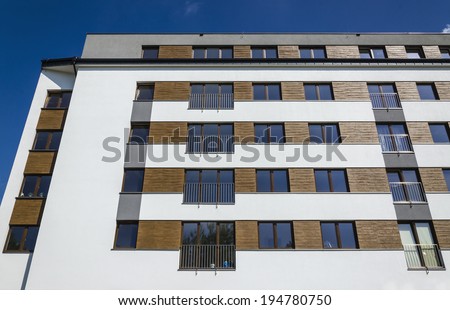 Architectural background of a modern stylish  apartment building, white facade decorated with wood against blue sky