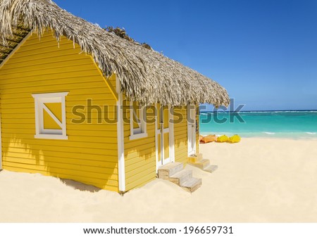 Wooden yellow hut on the beach covered with thatch against colorful kayaks, blue sky and azure water, Caribbean Islands